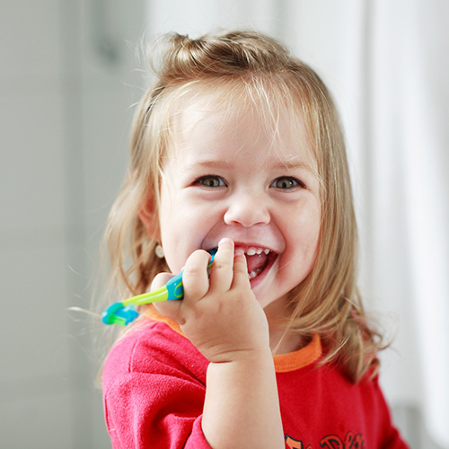 A toddler holding a toothbrush and smiling