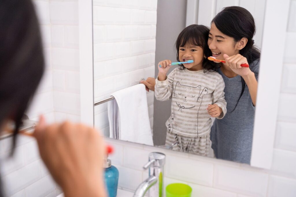 Mom teaching her daughter to brush her teeth in order to prevent toddler cavities