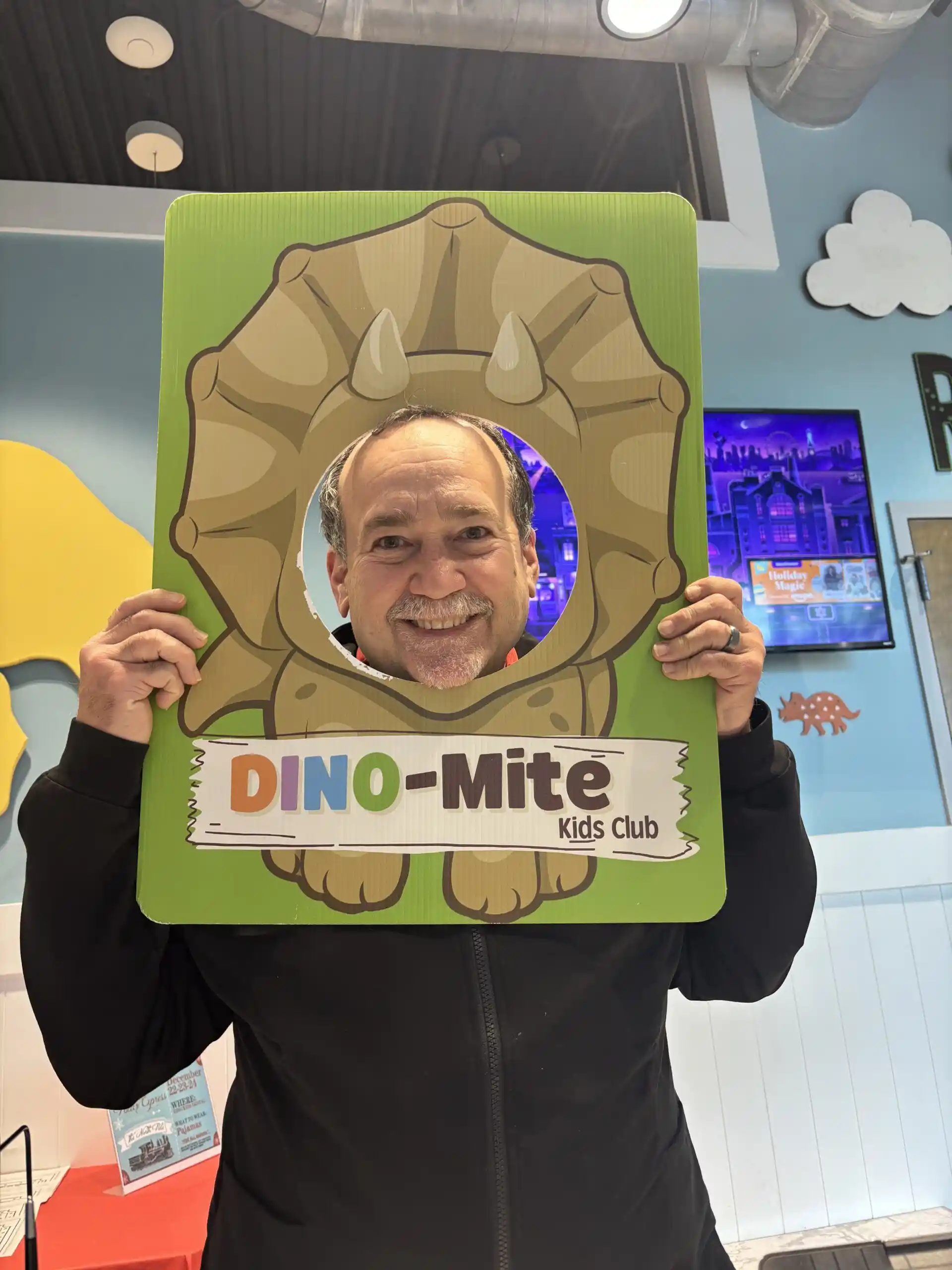 Dr. Carlos Garcia Soto posing playfully with a DINO-Mite Kids Club photo frame at Dino Kids Pediatric Dentists